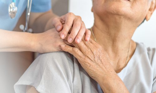 Closeup of older woman with healthcare worker's hand on her shoulder.