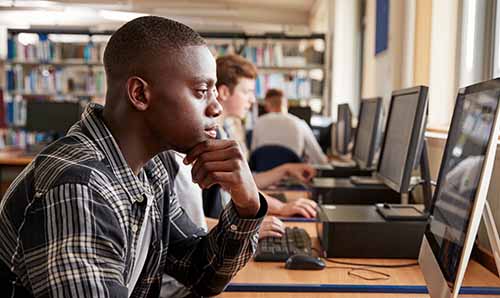 Young Black student working at computer in library